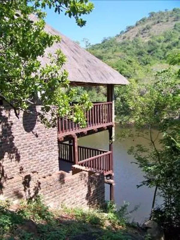 A brick house with a wooden balcony overlooking a lake and forested hills
