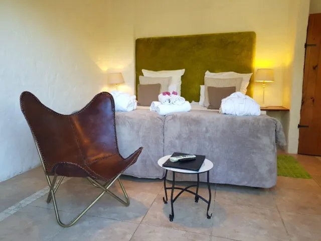Brown leather chair beside a neatly made bed with green headboard in a cozy room