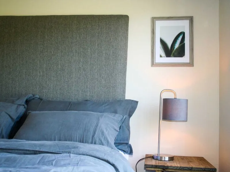 Modern bedroom with blue bedding headboard nightstand lamp and framed leaf art