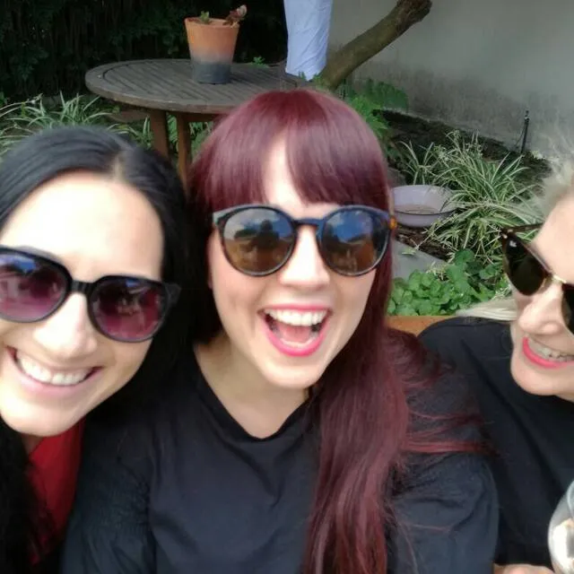 Three people with sunglasses smiling in a garden setting