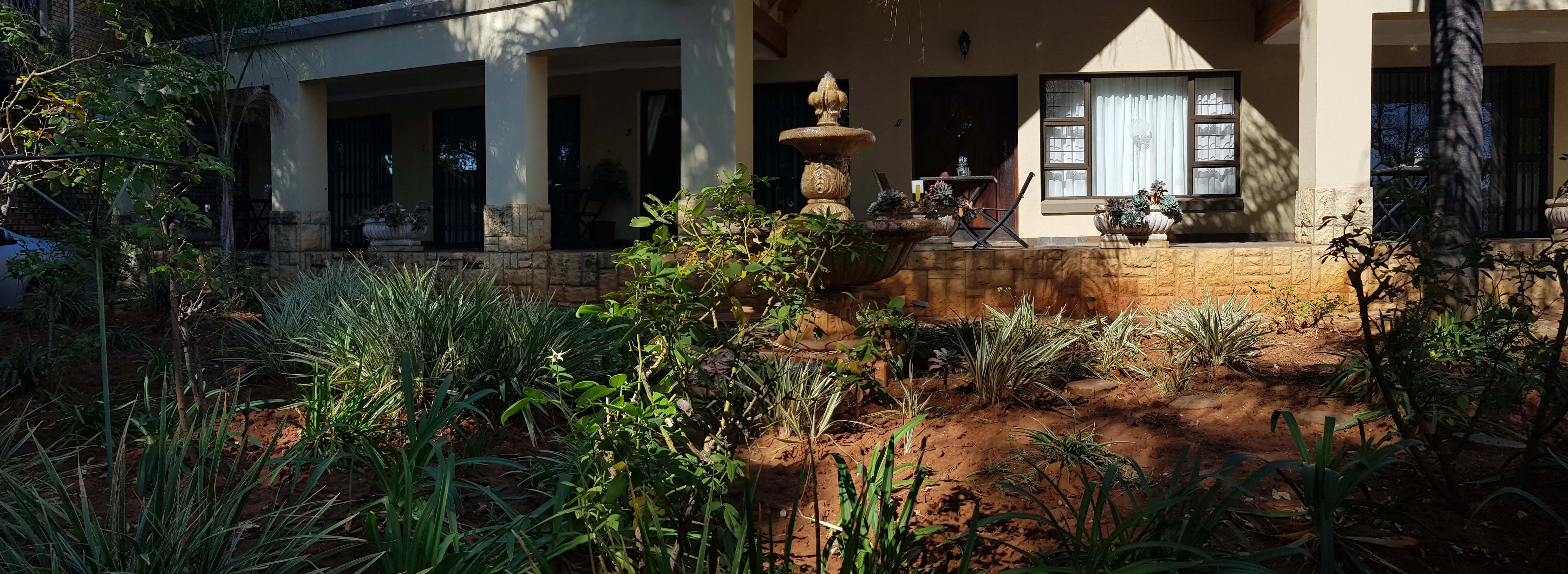 House with a garden featuring plants a fountain and a sunny patio