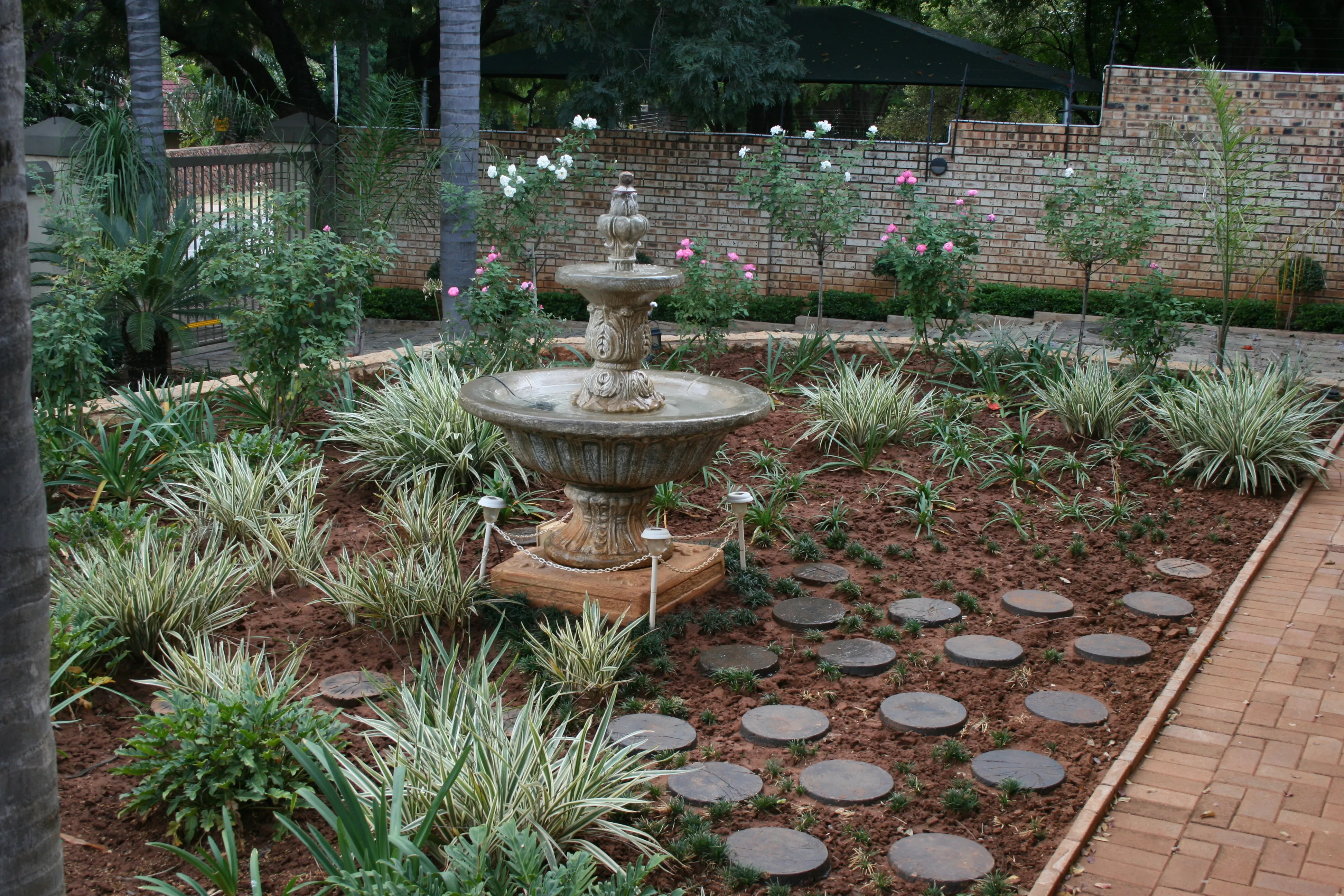 Stone fountain in a garden with variegated plants and stepping stones