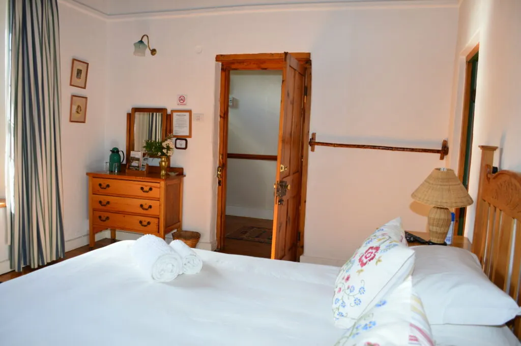 Bedroom with wooden door dresser bed with white linens and floral pillows