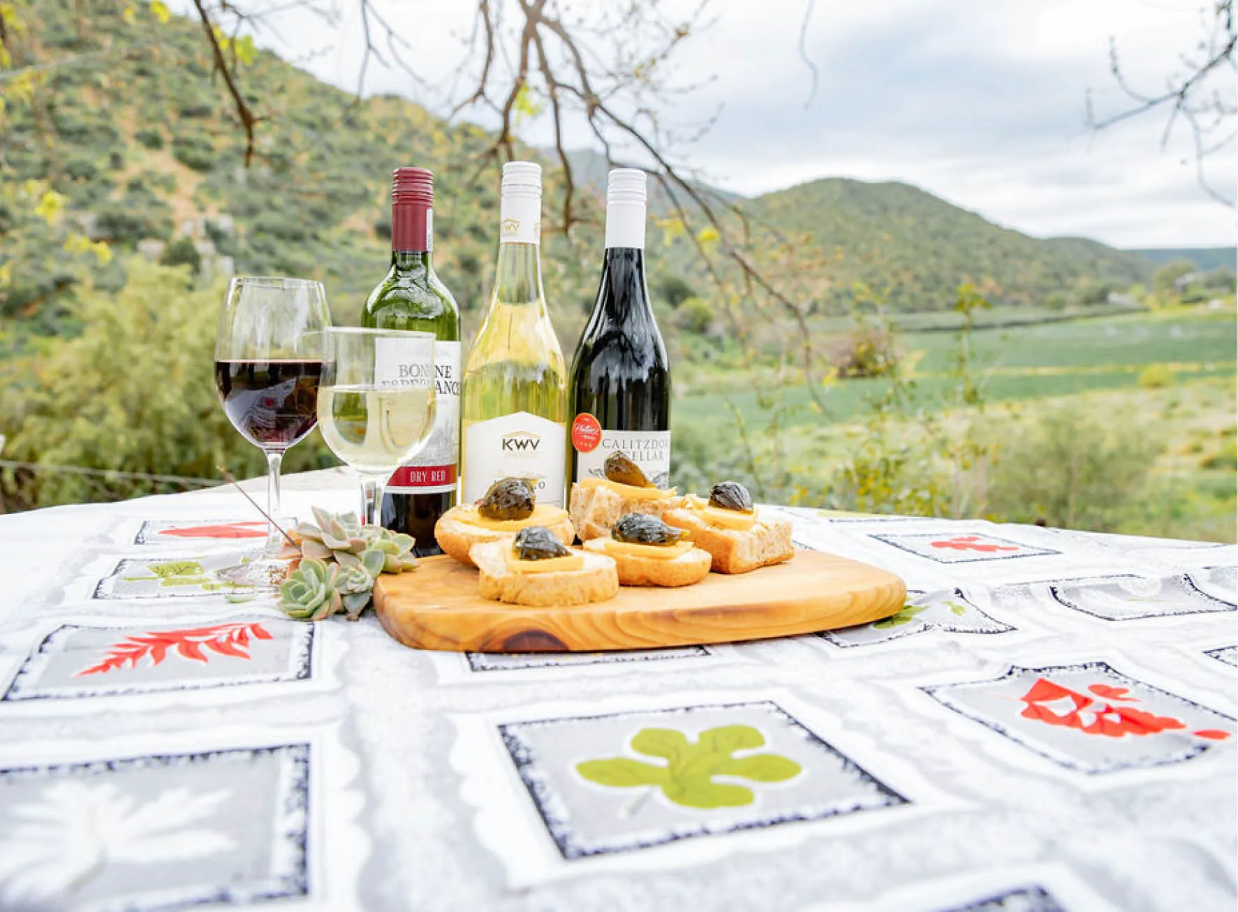 Four wine bottles glasses and bread on a table with a scenic background