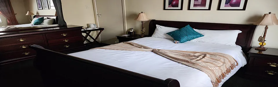 A neatly made bed in a bedroom with dark wood furniture and artwork
