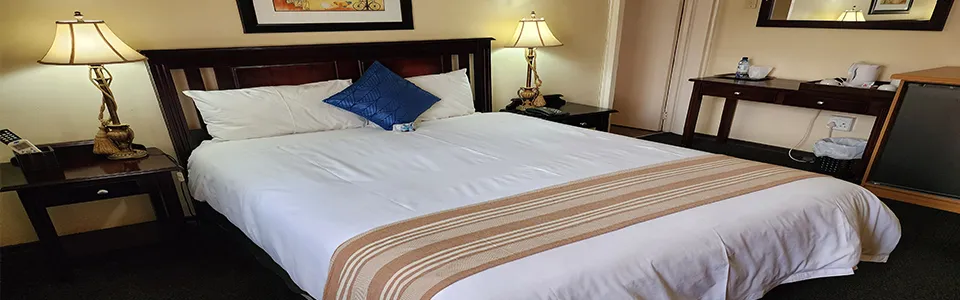 Neatly made bed in a hotel room with wooden furniture and lamps