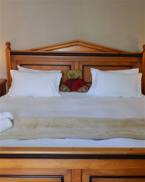 Wooden bed with white bedding two pillows and a teddy bear in the middle