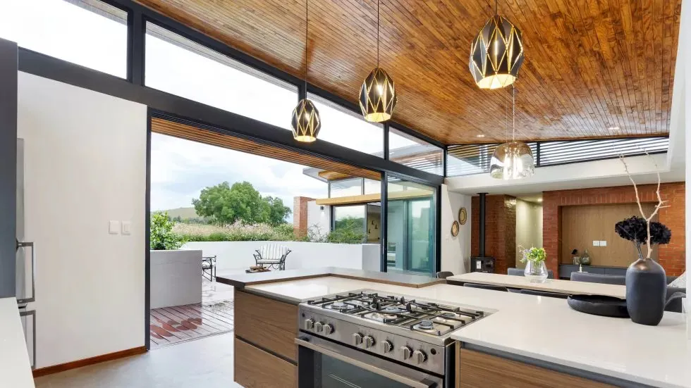 Modern kitchen with wooden ceiling open to outdoor patio with scenic view
