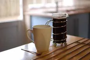 Coffee cup and French press on a wooden table in a kitchen