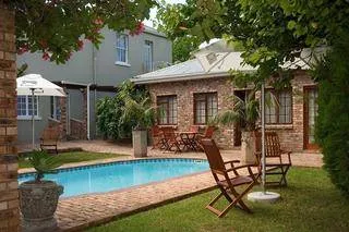 Swimming pool with lounge chairs and a brick building in a garden setting