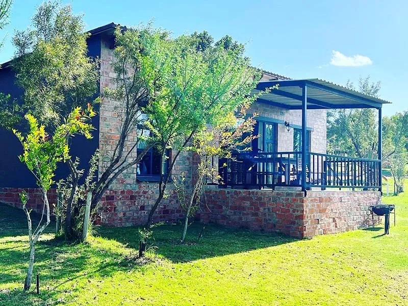 Brick cottage with a veranda surrounded by greenery under a blue sky