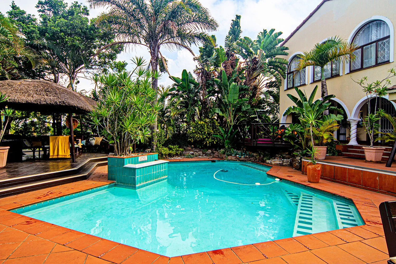 Swimming pool with tropical plants and a thatched hut in a courtyard