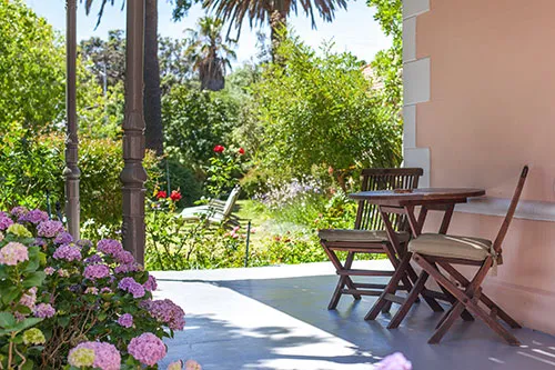 Wooden chairs and table on a patio with blooming flowers and lush greenery
