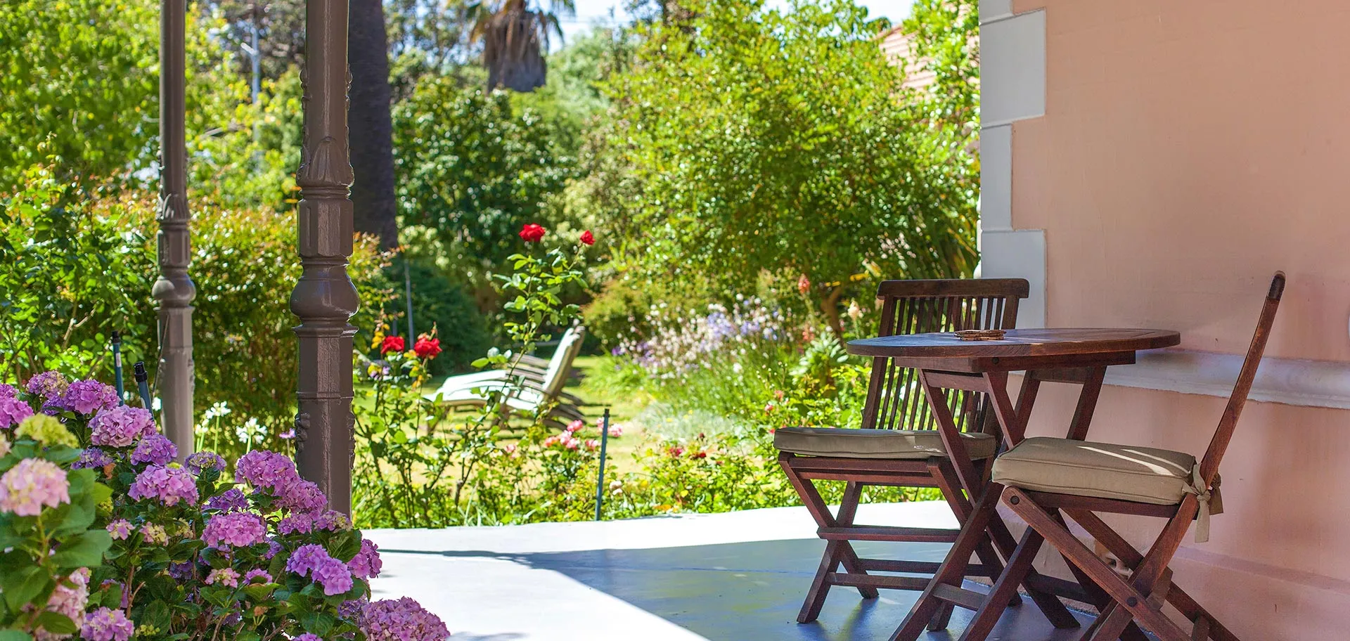 Wooden chairs and table on a patio with lush garden in the background