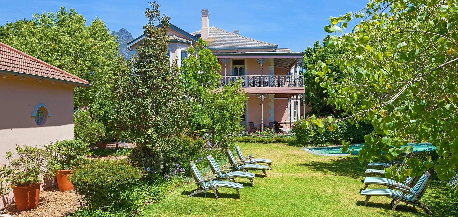 Garden with lounge chairs potted plants and a house in the background