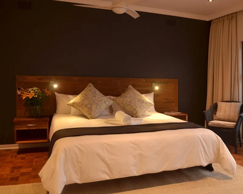 Large bed with pillows and flowers in a dimly lit bedroom with wooden floor