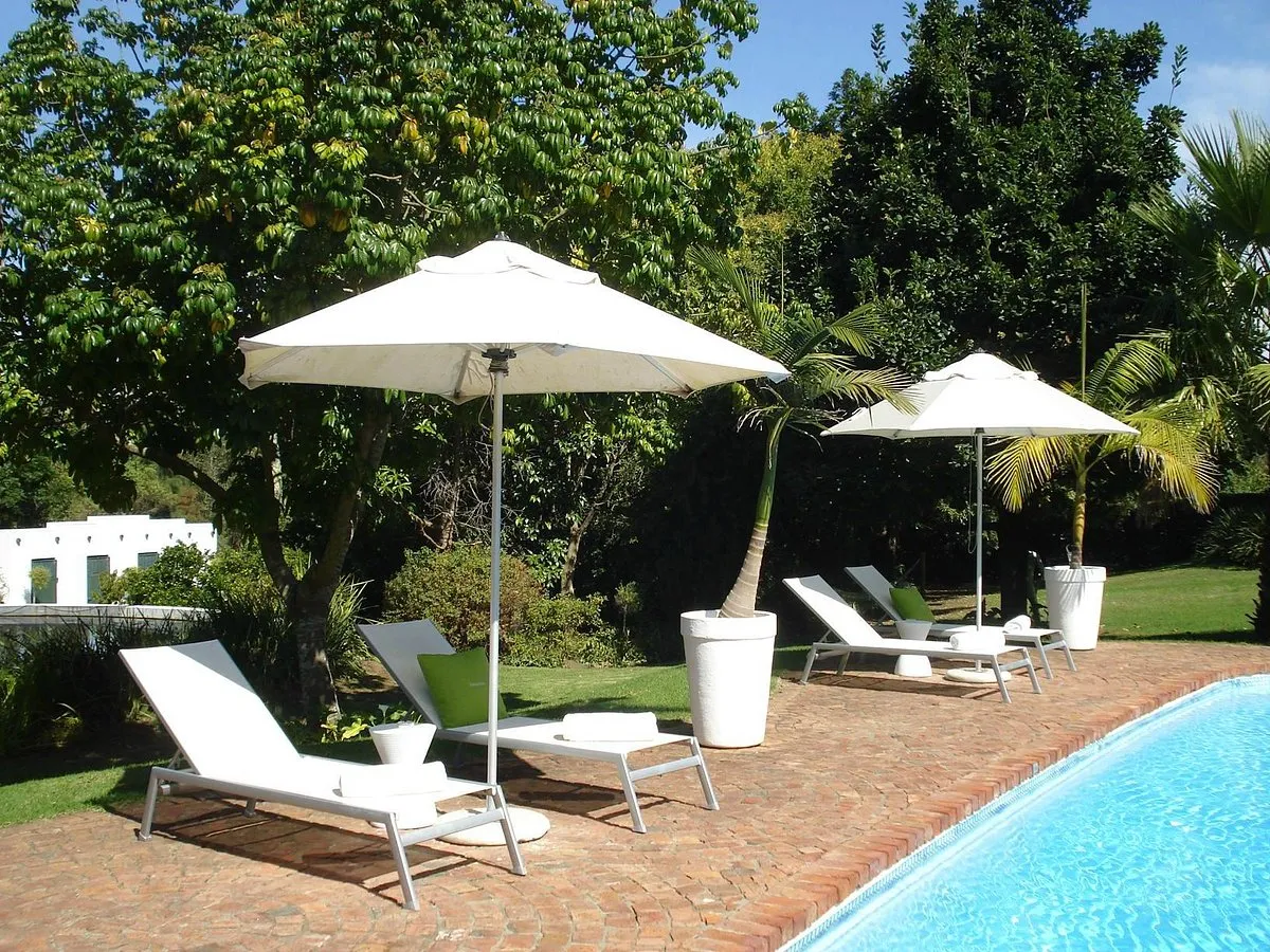 White lounge chairs with umbrellas by a pool in a lush garden setting