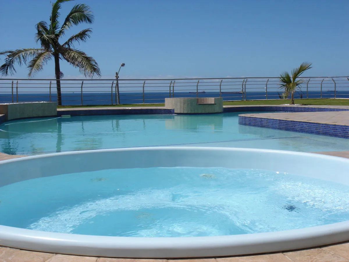 Swimming pool and hot tub with palm trees and ocean view in background