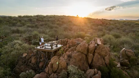 Elevated wooden deck on rocky hill with people enjoying sunset in a desert