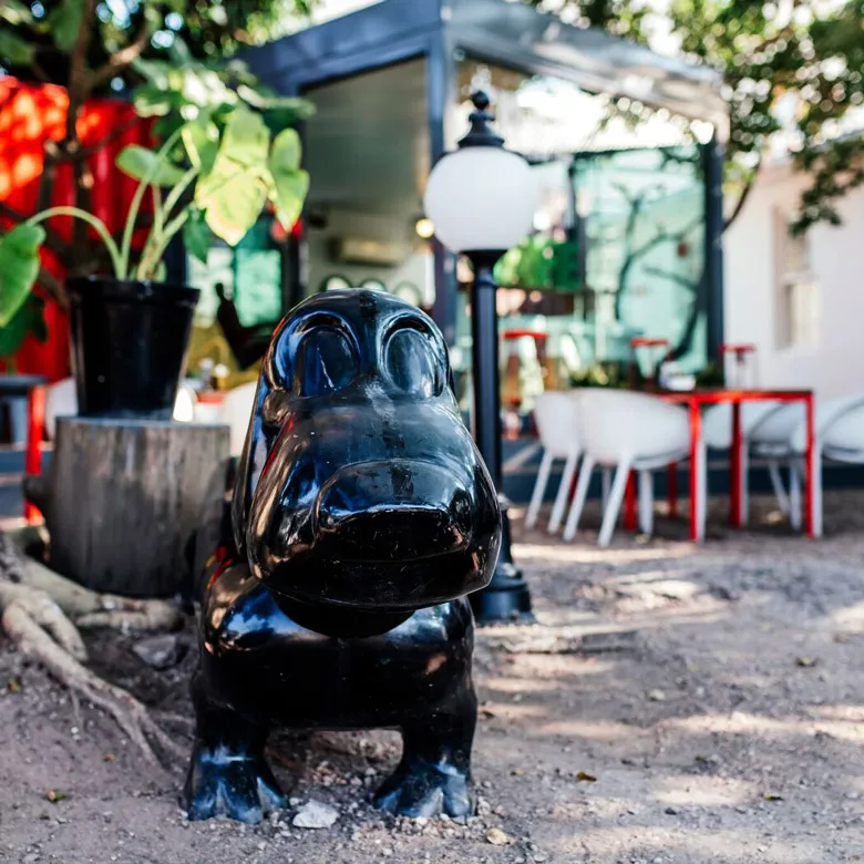 Black hippo statue in front of a modern outdoor caf with red chairs