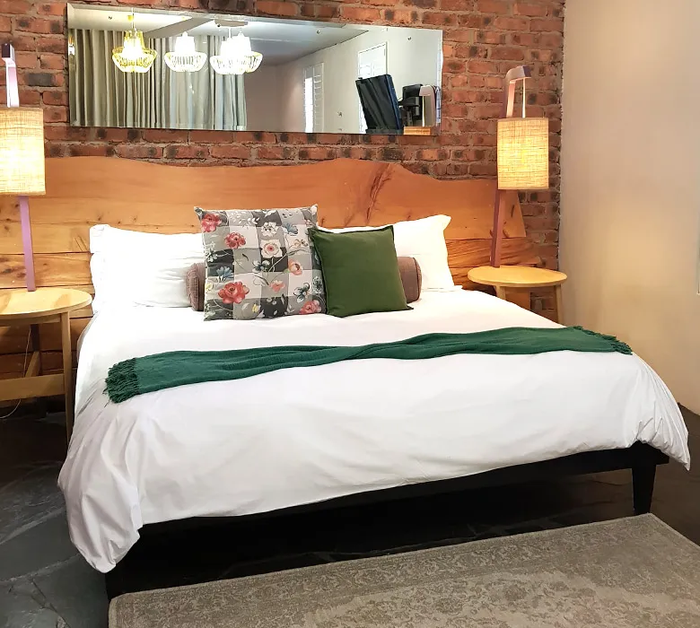 Wooden headboard white bed with green blanket brick wall and bedside lamps