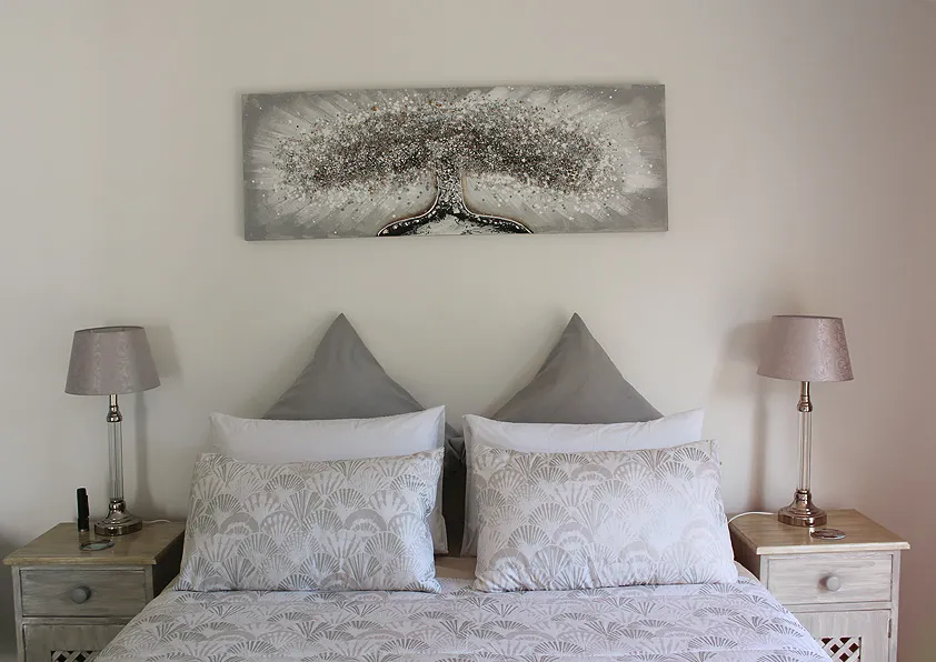 Bedroom with a neatly made bed two bedside lamps and a wall art piece