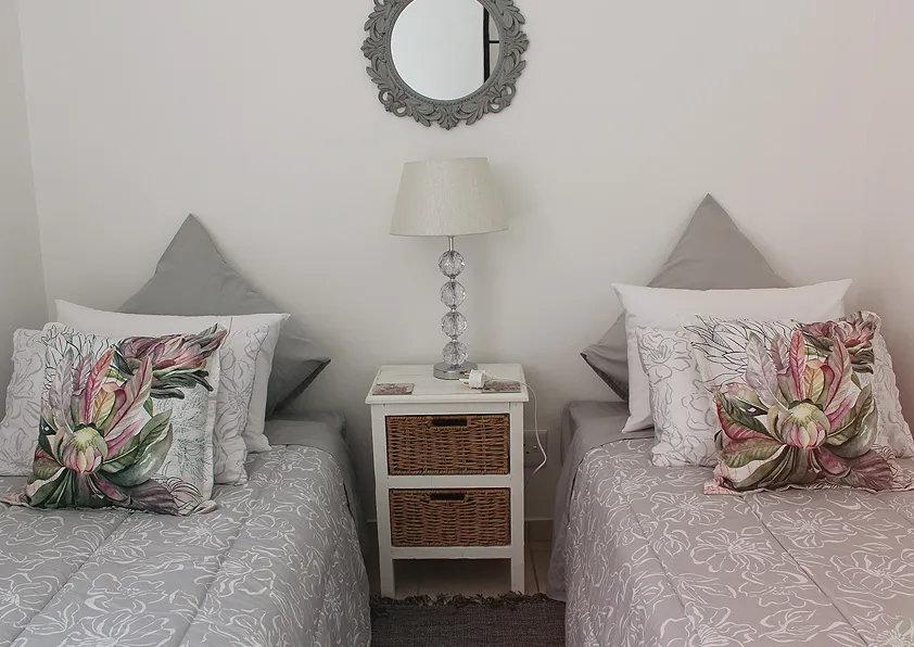 Two single beds with floral pillows bedside table and wall mirror in bedroom