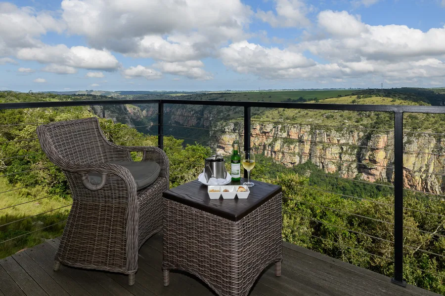 Wicker chair and table with wine on a wooden deck overlooking a canyon