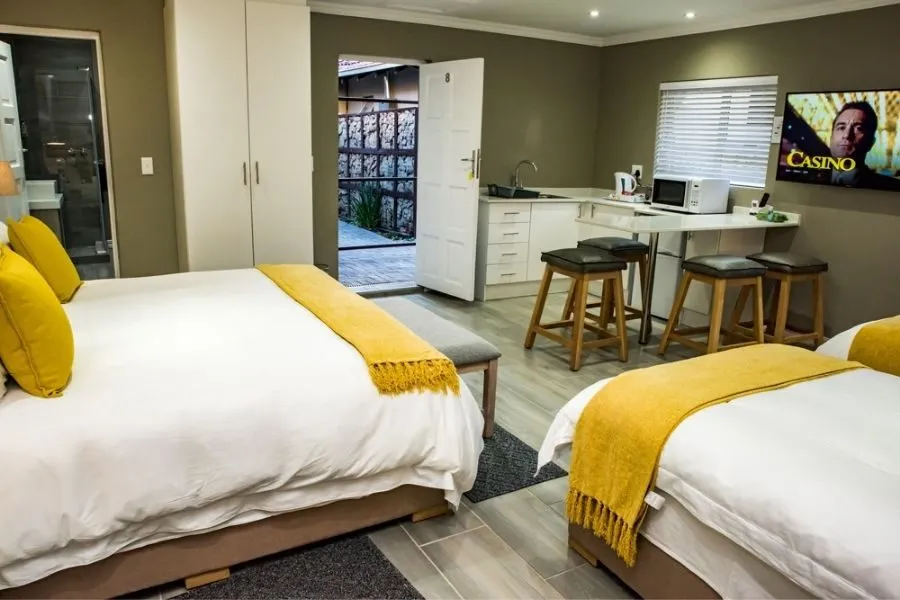 Bedroom with two beds kitchenette stools and a TV showing a movie