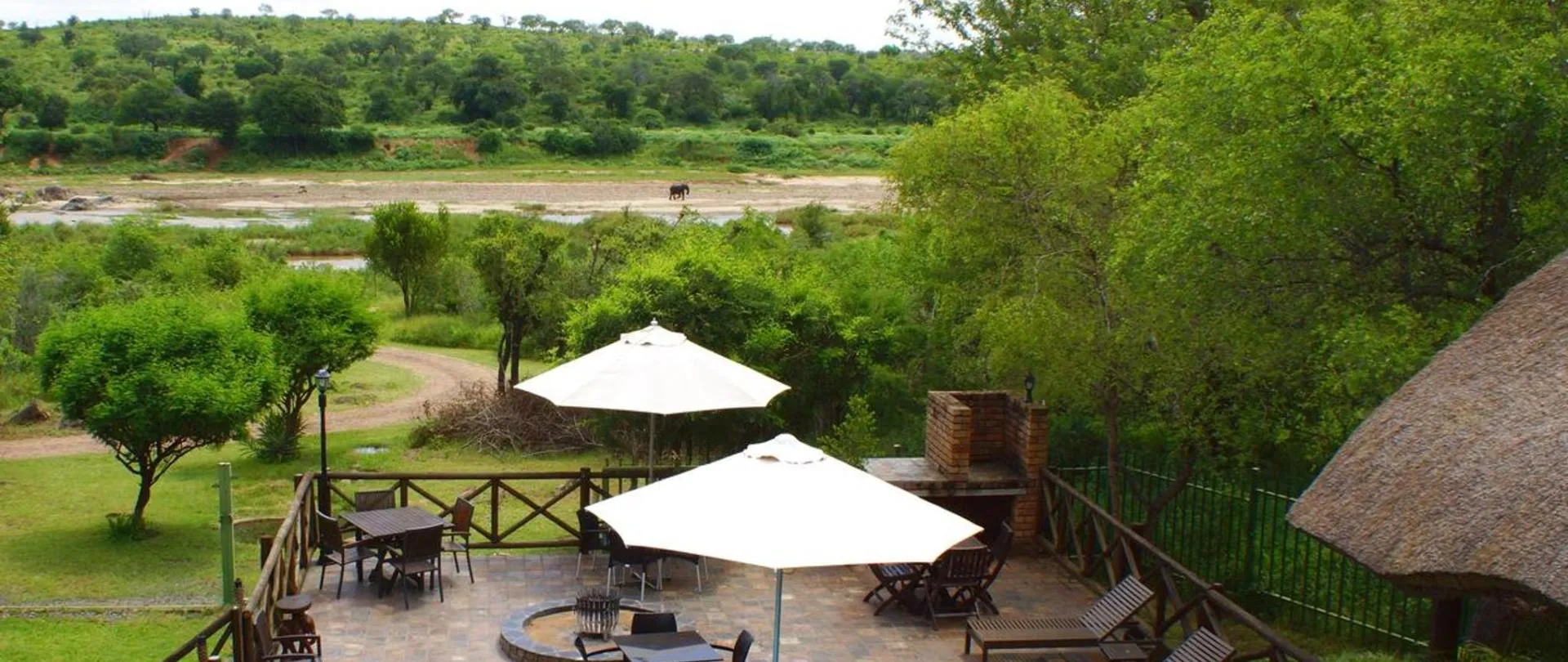Outdoor seating area with umbrellas overlooking a lush green landscape and river