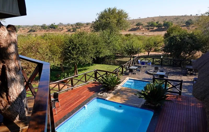 Wooden deck with blue pool green plants and outdoor seating overlooking a landscape