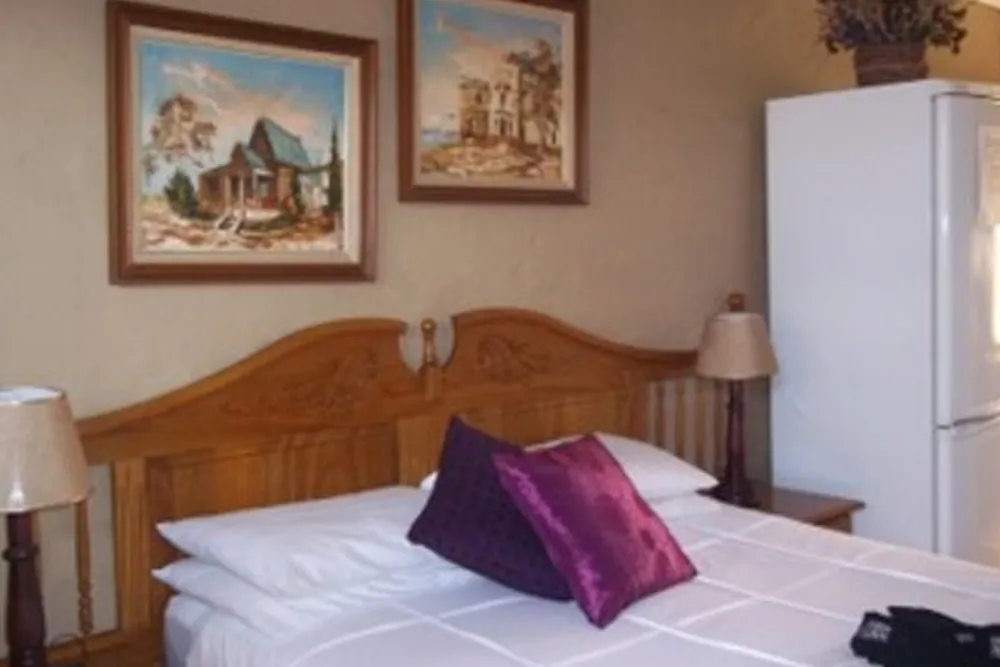 Wooden bed with white linens purple pillow two lamps and two paintings on beige wall