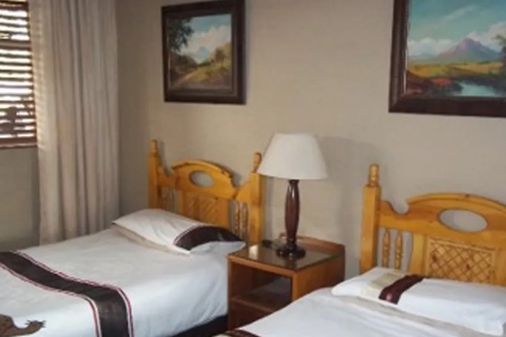 Two single beds in a bedroom with wooden headboards and landscape paintings on the wall