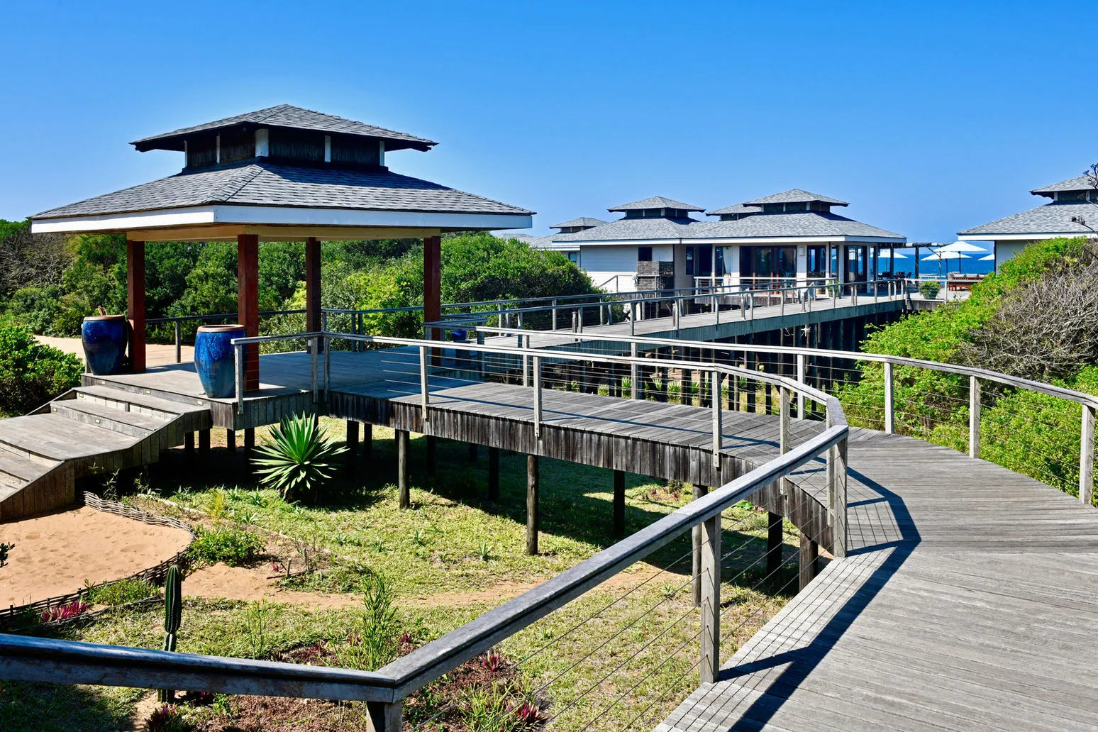 Elevated wooden walkways and buildings surrounded by greenery under a clear blue sky