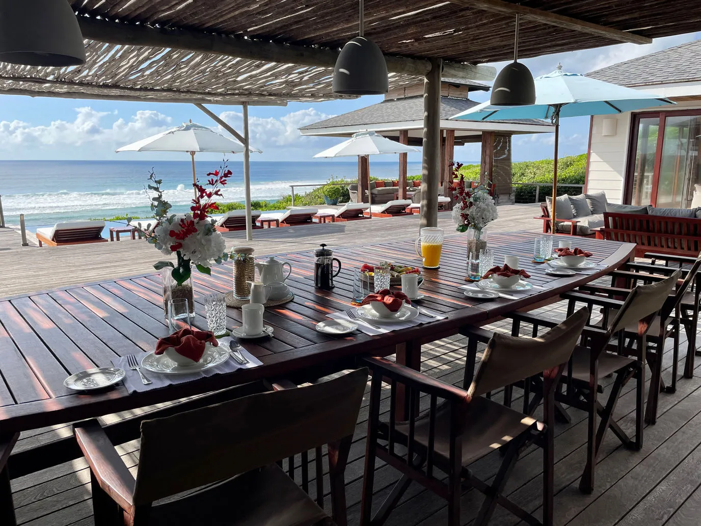 Wooden table set for breakfast with ocean view and umbrellas in the background