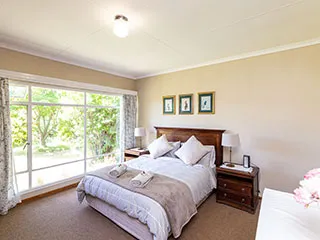 Bright bedroom with large windows neatly made bed and wooden furniture