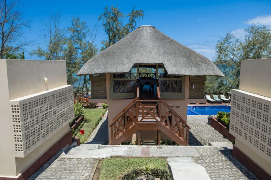 Beachfront bungalow with thatched roof wooden stairs and swimming pool in background