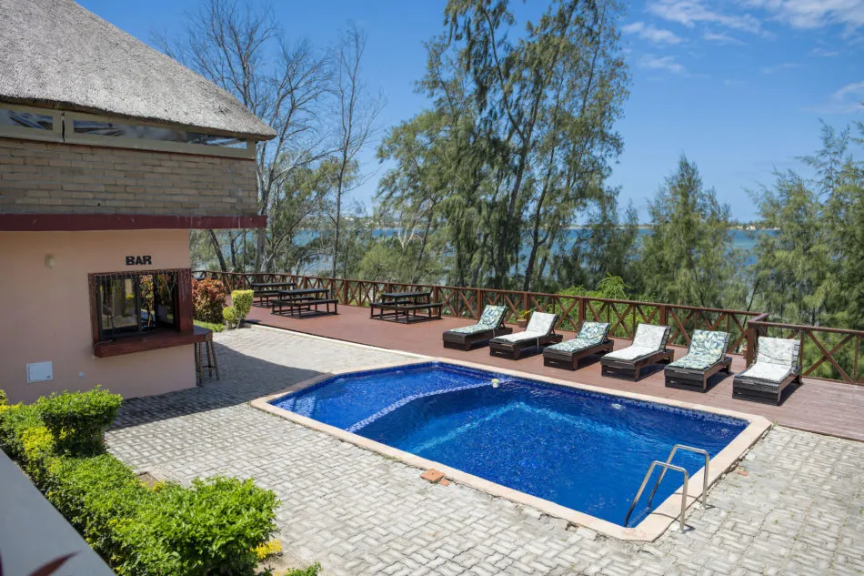 Swimming pool with lounge chairs overlooking a lake near a bar and trees