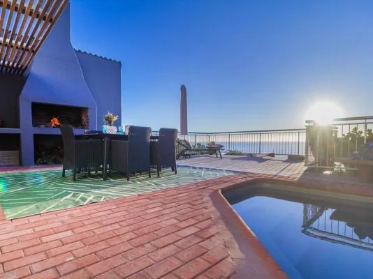 Outdoor patio with dining area pool and ocean view at sunset