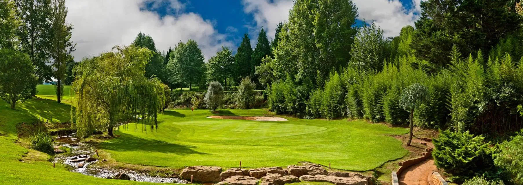 Lush green golf course with trees a stream and a blue sky