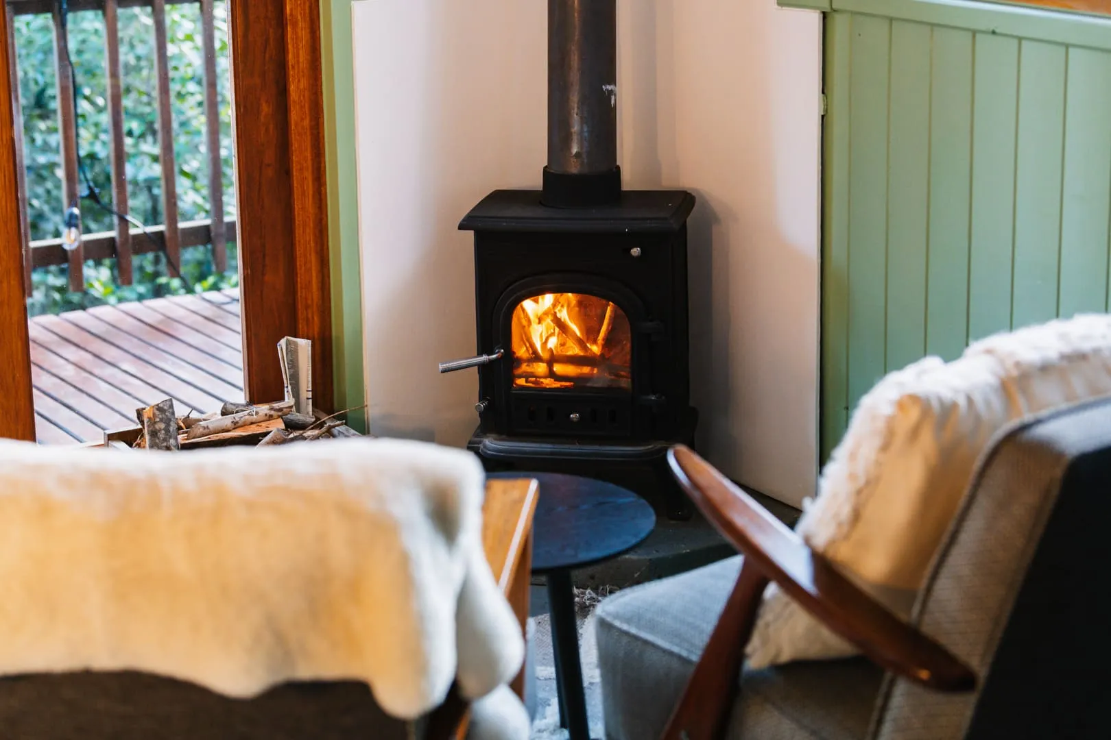 Cozy living room with lit fireplace chairs and wooden deck view