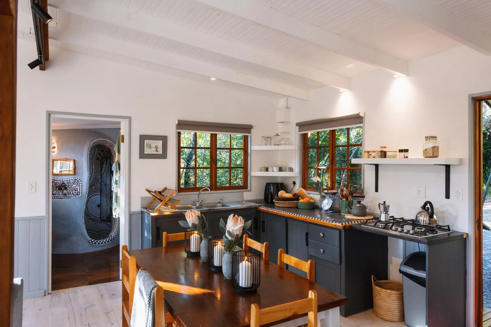 Cozy kitchen with wooden table chairs and large windows overlooking greenery
