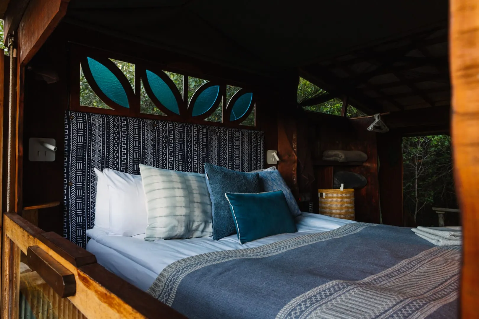 Cozy bed with blue and white pillows in a wooden cabin with stained glass