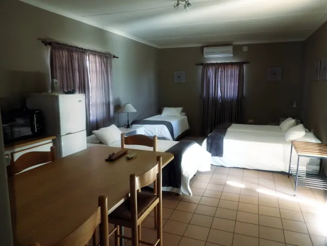 Small room with two single beds dining table fridge and curtains