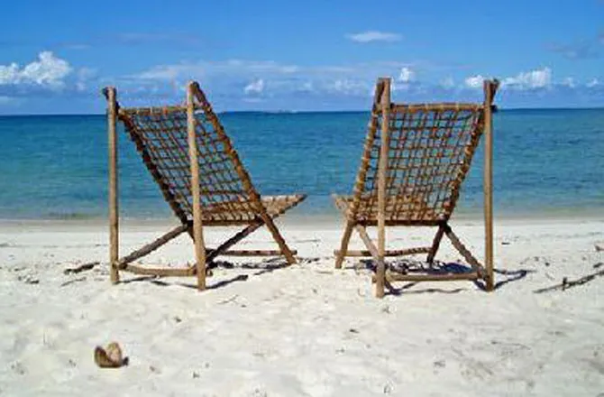 Two wooden lounge chairs on a sandy beach with the ocean in the background