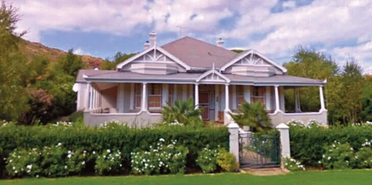 A large white house with a garden and a green lawn in front