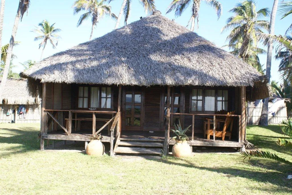 Thatchedroof wooden cabin with porch surrounded by palm trees and grass