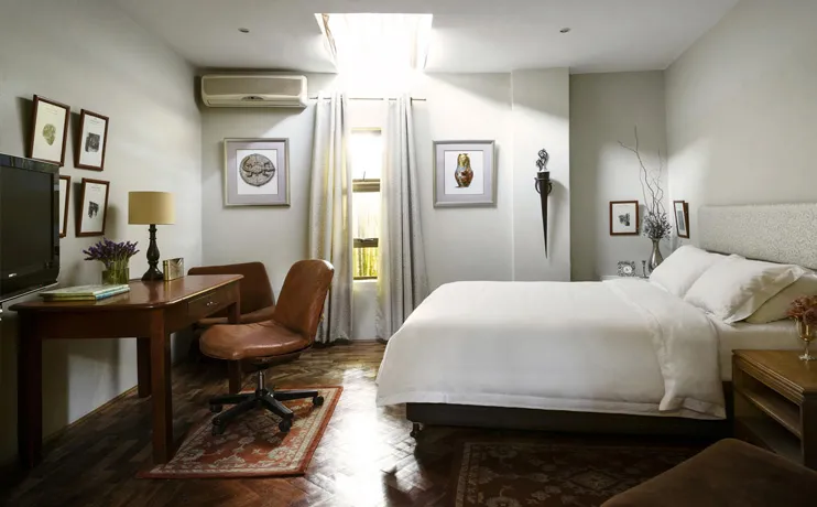 Cozy bedroom with a bed desk chair and wall art welllit by natural light