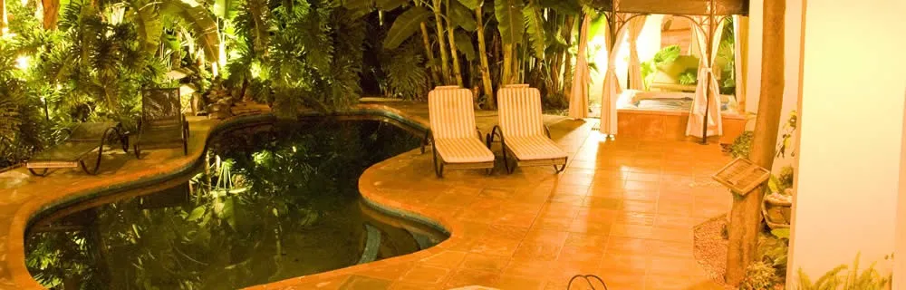 Outdoor pool area with lounge chairs lush greenery and warm lighting at night