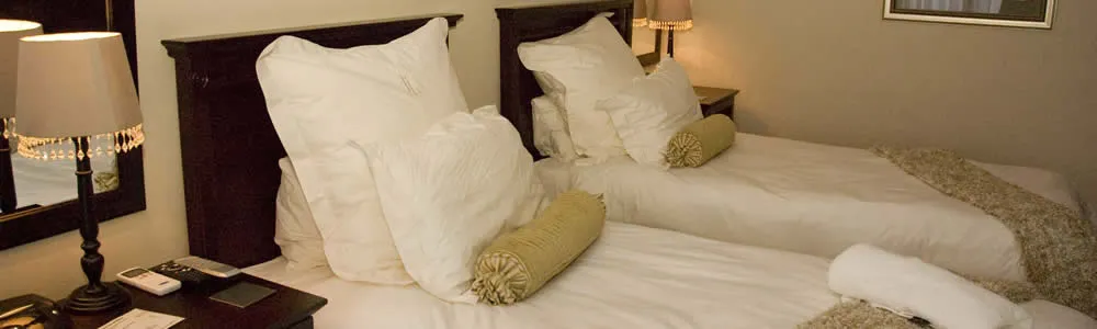 Two neatly made beds with white pillows and green cylindrical cushions in a bedroom